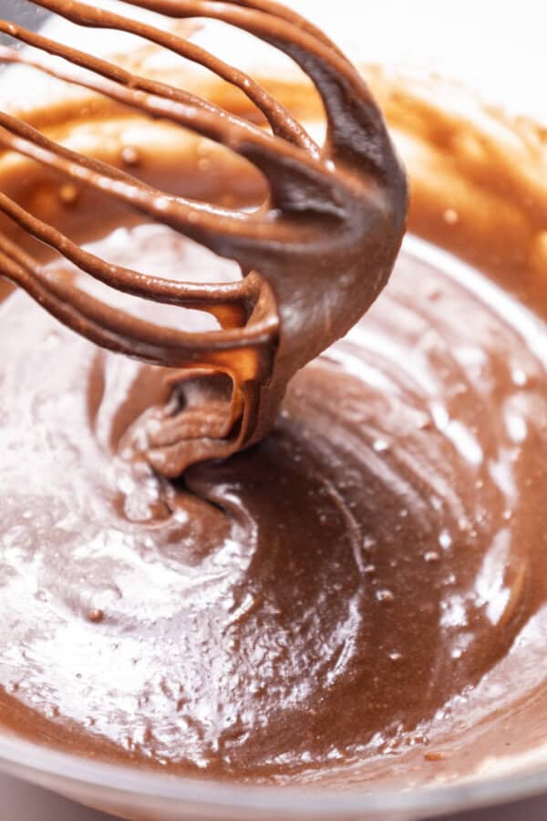 Brownie batter in a clear mixing bowl with a whisk.