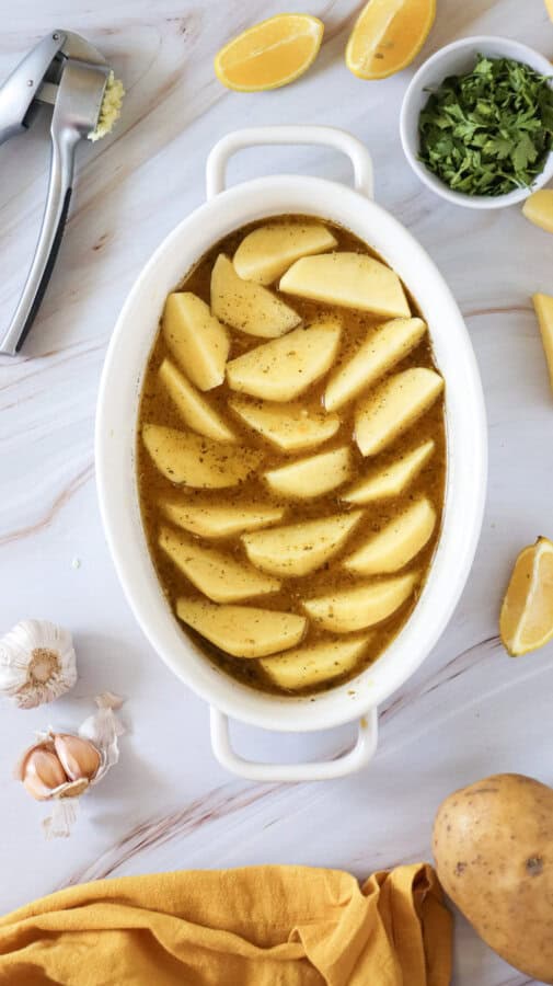 Sliced potatoes covered in a mixture in a white casserole dish.