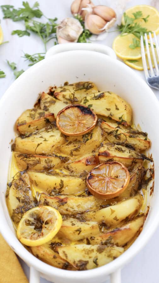 Lemon greek potatoes garnished with fresh parsley, in a white baking dish .