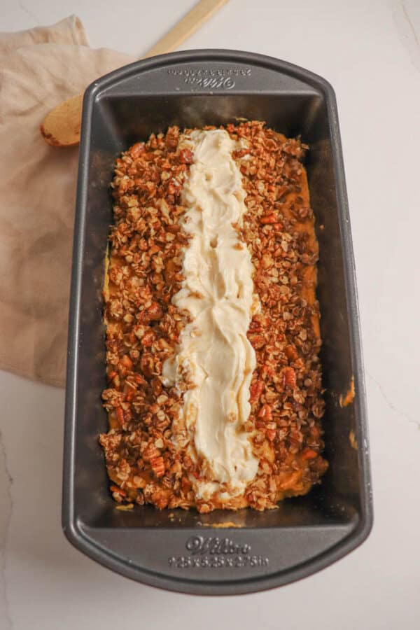 Pumpkin bread batter with a line of cream cheese down the center in a loaf baking dish.