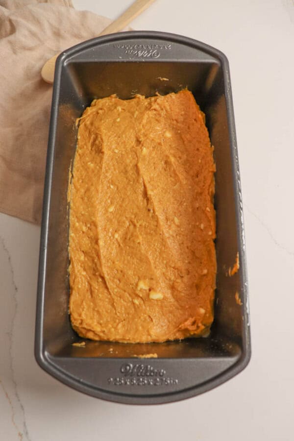 Pumpkin bread dough in a loaf pan on a white table.