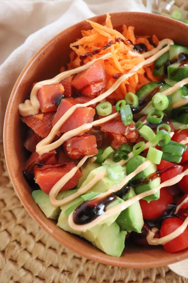 Orange bowl filled with smoked salmon cubes, diced cucumber, diced avocado and cherry tomatoes topped with spicy mayo.