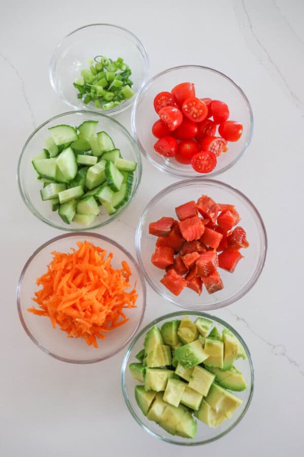 Ingredients for smoked salmon rice bowls in clear glass prep bowls on a white counter.