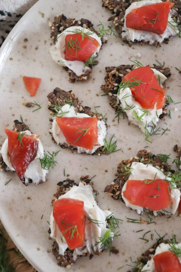 Crackers with cream cheese and pieces of smoked salmon garnished with fresh dill on a cream plate.
