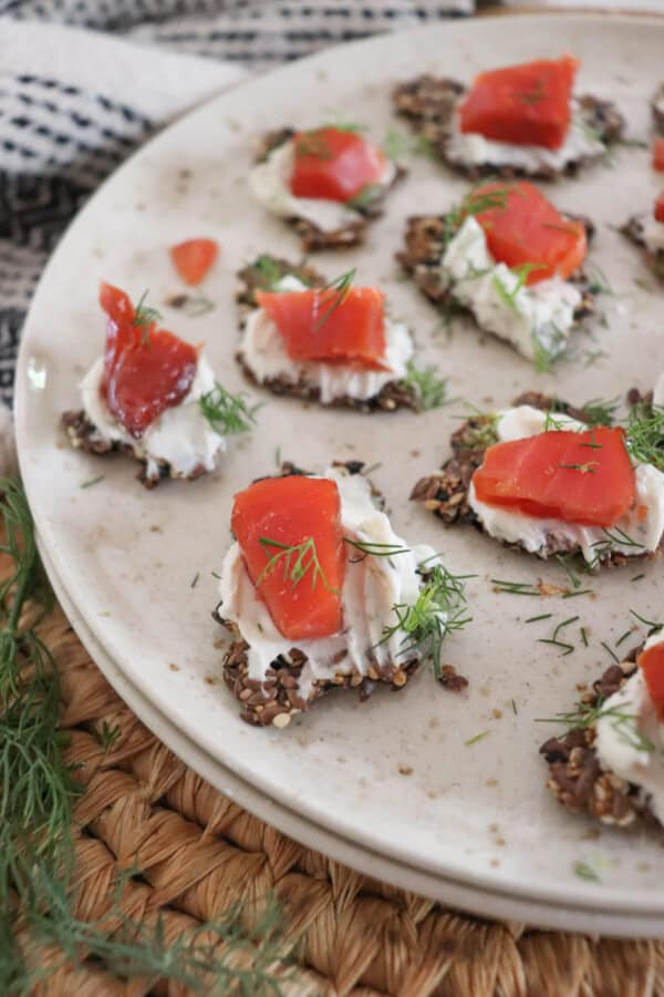 Crackers with cream cheese and pieces of smoked salmon garnished with fresh dill on a cream plate.