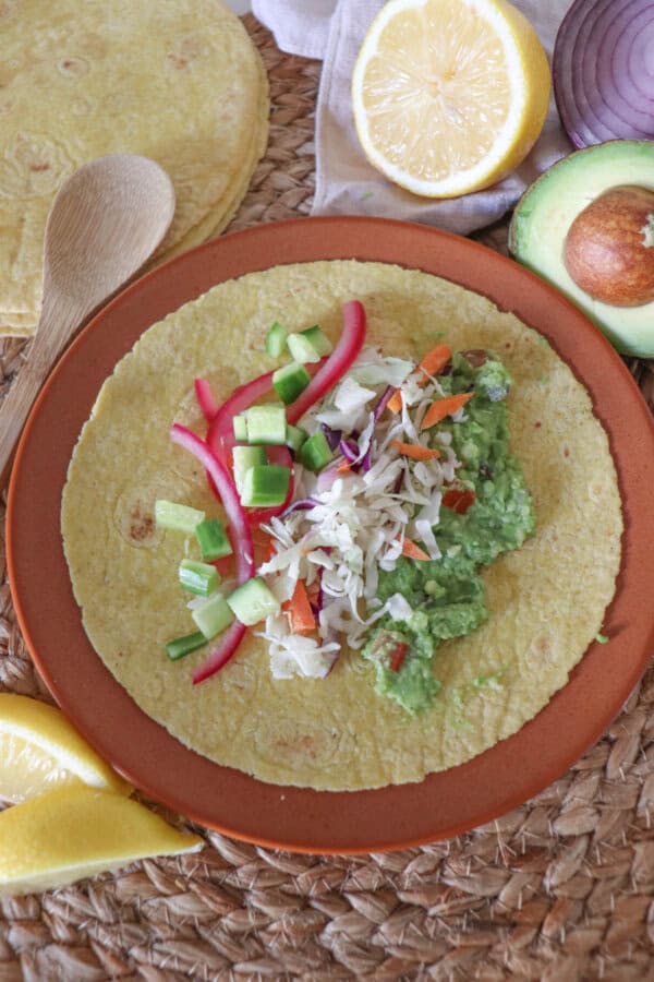 Open faced taco with diced cucumbers, pickled red onion, guacamole and garnished with dill and chives and cilantro lime crema on an orange plate.