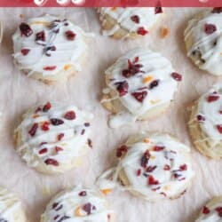 Top view of twelve cookies topped with white icing and sprinkled with dried cranberries and orange zest. They are arranged on a sheet of parchment paper. Text reads Cranberry bliss cookies and homemadeheather.com.