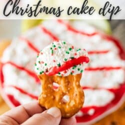 A hand holding a dipped pretzel with whipped topping and red and green sprinkles, with a plate of Christmas cake dip in the background. Text reads Little Debbie Christmas cake dip at the top and homemadeheather.com at the bottom.