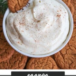 A bowl of creamy eggnog dessert dip sprinkled with nutmeg is surrounded by ginger snap cookies. One cookie is partially dipped in the bowl. Greenery decorates the upper left corner, and a red plaid fabric is visible in the background.