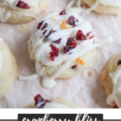 Close-up of cookies topped with white icing and sprinkled with dried cranberries and orange zest. The text at the bottom reads cranberry bliss cookie recipe homemadeheather.com.