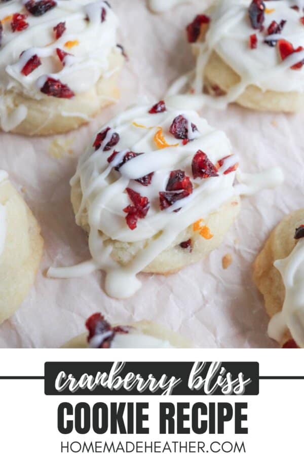 Close-up of cookies topped with white icing and sprinkled with dried cranberries and orange zest. The text at the bottom reads cranberry bliss cookie recipe homemadeheather.com.