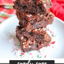 A stack of candy cane brownies on a white plate, topped with crushed candy cane pieces, with a festive red and green background. Text reads Candy Cane Brownie Recipe - homemadeheather.com.