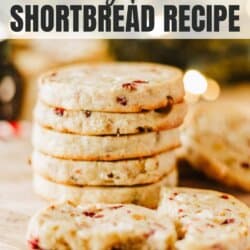 Stack of cranberry pistachio shortbread cookies on a wooden board, with more cookies in the background. Text overlay reads, Cranberry Pistachio Shortbread Recipe.