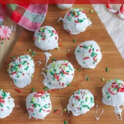 A wooden board with white chocolate-covered Oreo balls decorated with festive red and green sprinkles, surrounded by a red and green checkered cloth and Christmas-themed decorations.