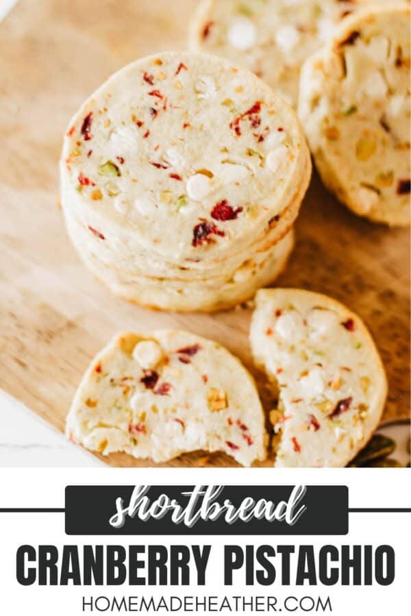 A stack of cranberry pistachio shortbread cookies on a wooden surface. The cookies are speckled with visible pieces of cranberries and pistachios. Text at the bottom reads shortbread cranberry pistachio homemakeheather.com.