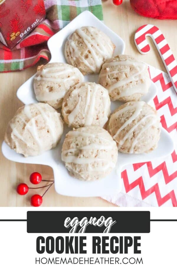 A star-shaped plate holds six eggnog cookies drizzled with icing. The plate is on a wooden surface with festive red berries, a candy cane, and a red and green cloth nearby. Text reads Eggnog Cookie Recipe - homemadeheather.com.