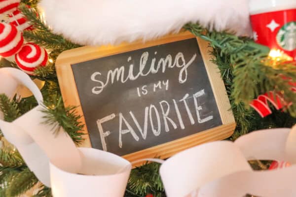 A festive Christmas tree adorned with a small chalkboard sign reading Smiling is my favorite. The tree is decorated with paper chains, striped candy ornaments, and a red cup bearing a Starbucks logo.