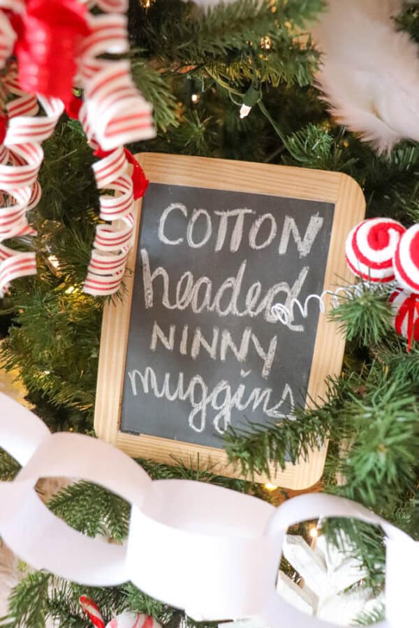 A Christmas tree decorated with red and white candy cane ornaments, white paper chains, and a chalkboard sign with the words Cotton headed ninny muggins written on it.