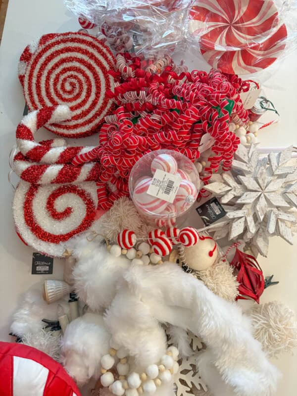 A collection of Christmas decorations on a table, including red and white spiral ornaments, candy cane patterns, a large wooden snowflake, red and white ribbons, peppermint swirls, and fluffy white garlands.