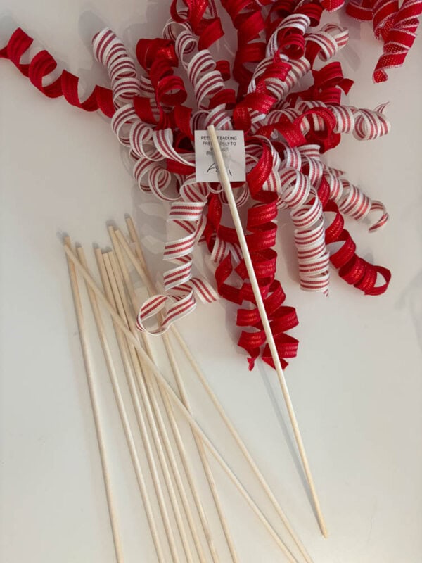 Red and white curly ribbons attached to long wooden sticks are laid out on a white surface. A small tag with text is visible among the ribbons.
