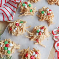 Festive no-bake cookie clusters on parchment paper, decorated with red, green, and white candies. A red and white striped cloth and candy canes are nearby, adding to the holiday theme.