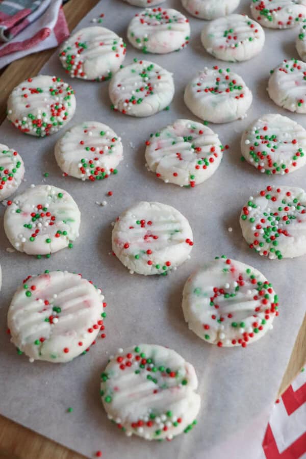 A batch of festive cookies on parchment paper, decorated with red, green, and white sprinkles.