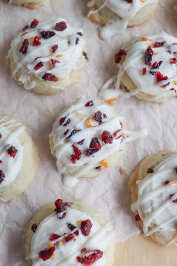 Close-up of cookies topped with white icing and dried cranberries, arranged on parchment paper. The cookies are drizzled with icing and sprinkled with small pieces of cranberries, creating a festive and appetizing appearance.