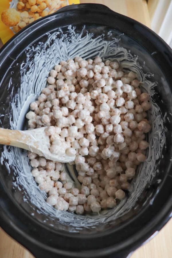A crockpot filled with cereal coated in melted marshmallows. A wooden spoon is partially visible, used for stirring the mixture.