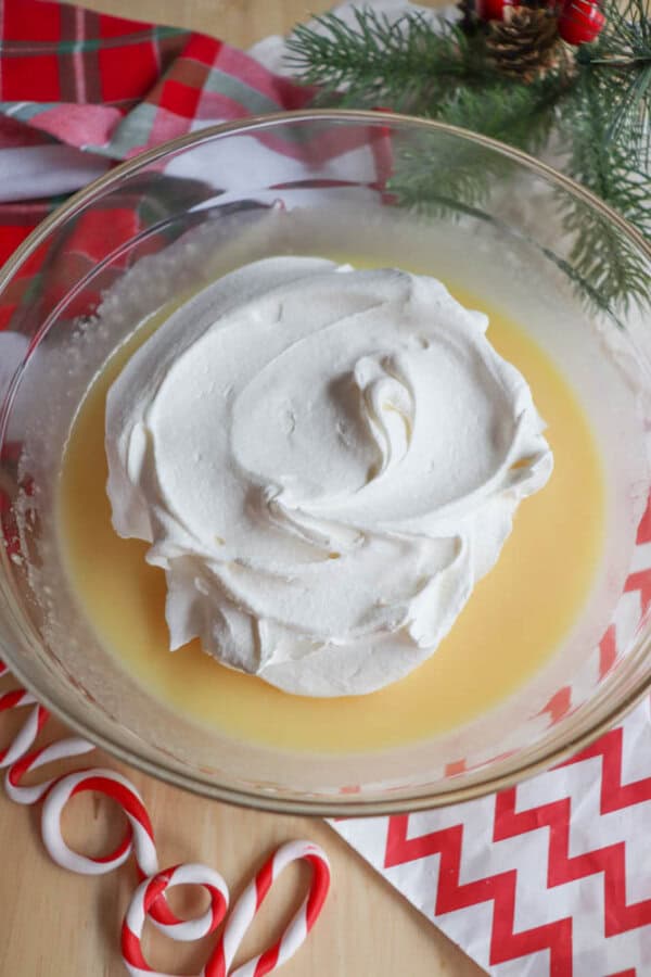 Eggnog and instant pudding mixture in a glass bowl, topped with a pile of whipped topping.