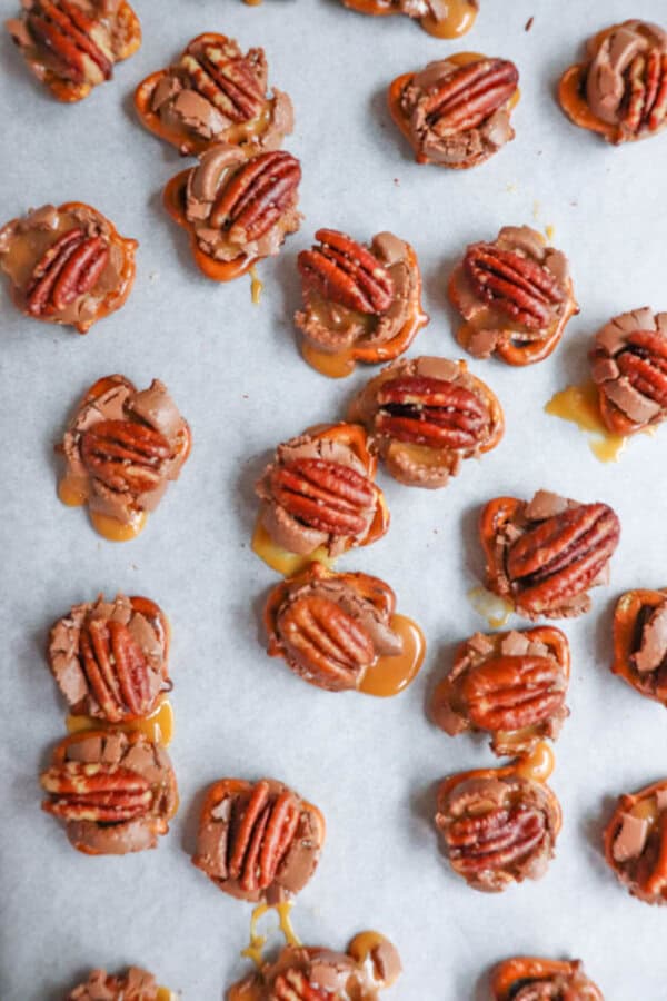 Small clusters of chocolate, caramel, and pecans are arranged on parchment paper. Each cluster is topped with a pecan and has a glossy, tempting appearance.