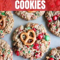 A tray of delightful Christmas kitchen sink cookies adorned with vibrant candies, pretzels, and oats sits invitingly on a baking sheet. Text overlay proclaims: Christmas Kitchen Sink Cookies.