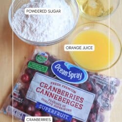 Ingredients on a table: a bag of fresh cranberries ready for your cranberry candy recipe, a bowl of powdered sugar, a glass of Prosecco, and a glass of orange juice.