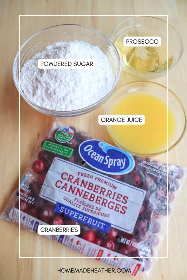 Ingredients on a table: a bag of fresh cranberries ready for your cranberry candy recipe, a bowl of powdered sugar, a glass of Prosecco, and a glass of orange juice.