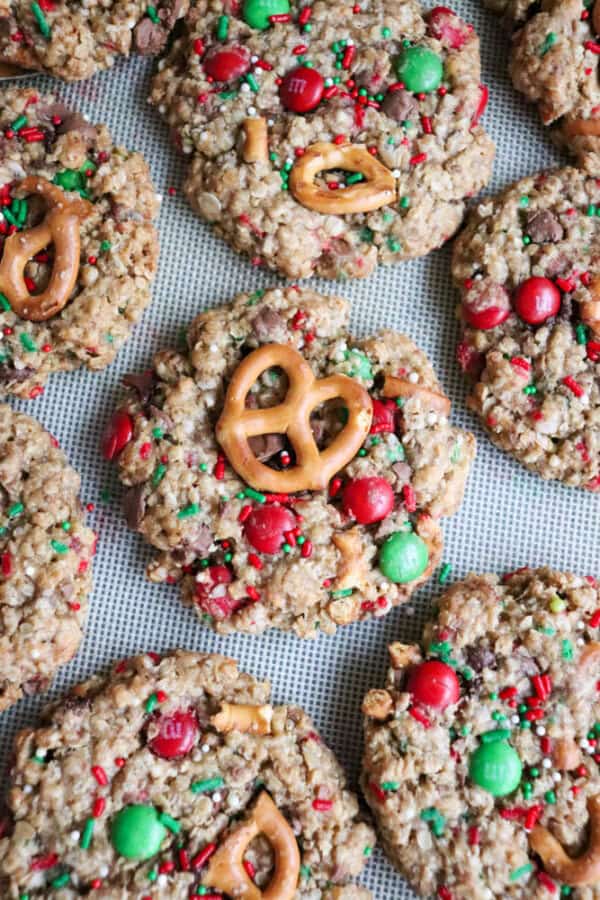 Christmas kitchen sink cookies burst with festive flair as colorful sprinkles, red and green candies, and mini pretzels adorn the oatmeal cookie base. Arranged on a baking sheet, these treats bring holiday cheer to any celebration.