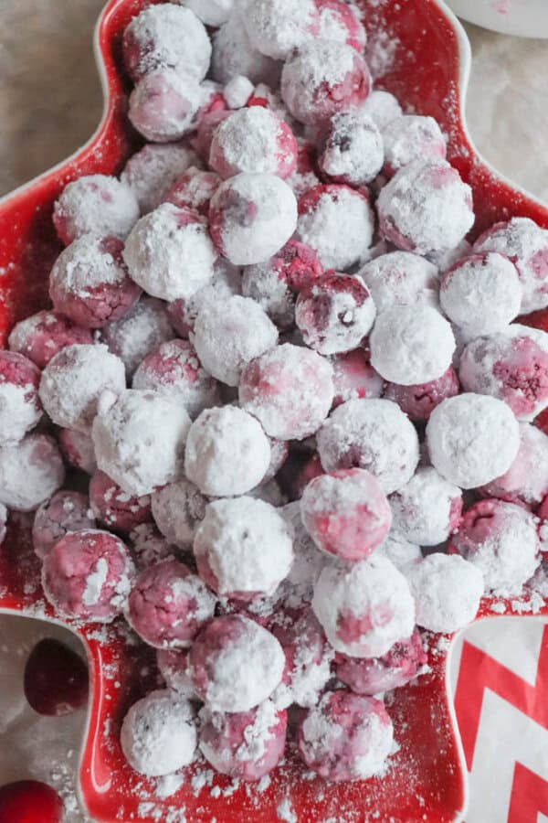 A red star-shaped plate filled with sugared cranberries resembles a cranberry candy recipe, coated in a layer of white powdered sugar. The bright red color of the cranberries peeks through the sugar, creating a festive and wintry appearance.