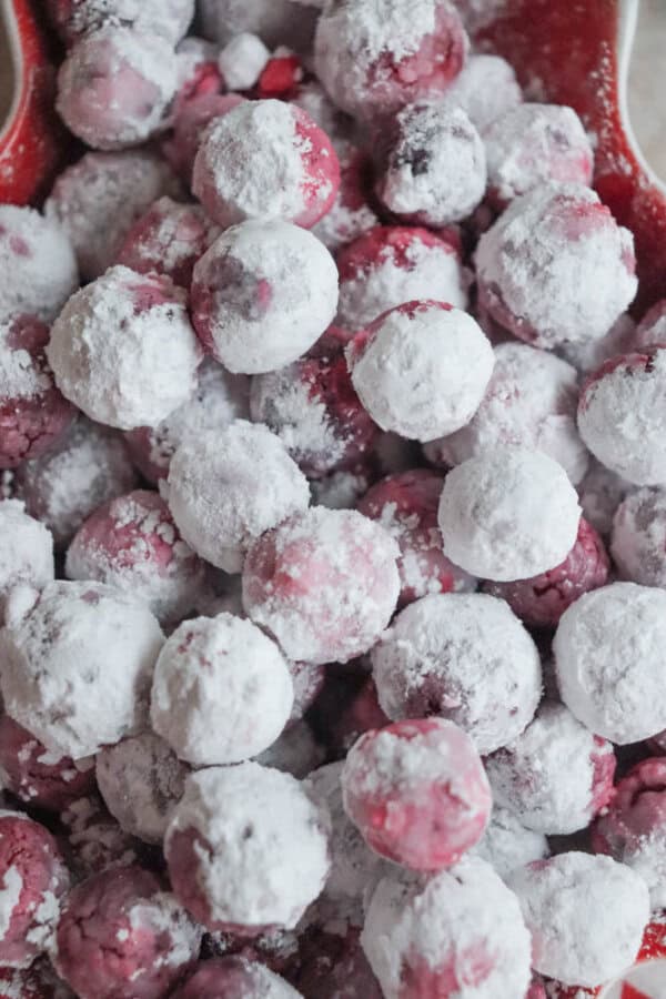 A close-up of cranberries coated in white powdered sugar, creating a festive and wintry appearance reminiscent of a classic cranberry candy recipe. The red berries peek through the white coating, giving a frosty, textured look.