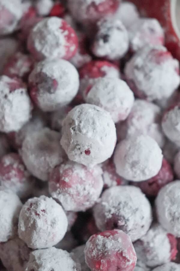 A close-up of frozen cranberries coated in a layer of white sugar evoke images from a cranberry candy recipe. The berries, piled randomly, showcase their round shape and the striking contrast between the deep red and bright white.