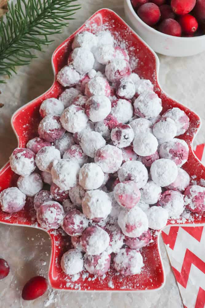 Experience the joy of a festive tree-shaped dish brimming with cranberries, dusted in powdered sugar like a delicate cranberry candy. A bowl of fresh cranberries and a green pine branch accentuate the holiday theme perfectly.