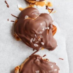Three delicious date bites topped with melted chocolate and sea salt sit on parchment paper. The text above reads 3-INGREDIENT chocolate coconut date bars in large letters, while the bottom displays the website name homemadeheather.com.