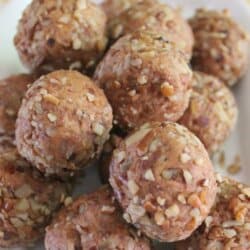 A close-up of a white plate piled with no-bake date balls. The balls are coated with crushed nuts. The top of the image includes text that reads No Bake Date Balls with a website URL: homemadeheather.com.