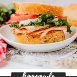 A delicious sandwich on homemade bread, stacked with turkey slices, lettuce, tomato, and a dollop of mayonnaise on a white plate. The background features fresh ingredients, and the text homemade sandwich bread along with a website URL is displayed.