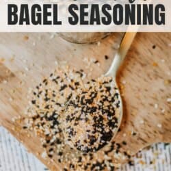 A spoonful of homemade bagel seasoning on a wooden board, with a mix of black and white seeds, salt, and spices. A small jar of seasoning in the background. The text reads homemade bagel seasoning and homemadeheather.com.