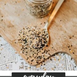 A jar and spoon filled with bagel seasoning sit on a wooden board. Some seasoning is scattered around the spoon. The text reads Everyday Bagel Seasoning and homemadeheather.com at the bottom.