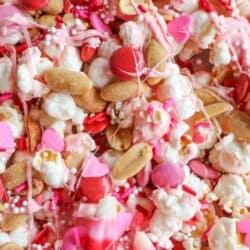 A colorful mix of popcorn, peanuts, pink and red candy-coated chocolates, and heart-shaped sprinkles is shown. The image is overlaid with Valentines Day Popcorn at the top and homemadeheather.com at the bottom, reminiscent of chocolate coconut date bars delightful texture.