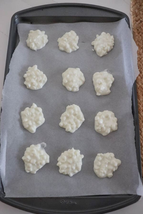 Twelve dollops of a white, creamy mixture, reminiscent of cottage cheese, are placed on a parchment-lined baking sheet, ready for baking.