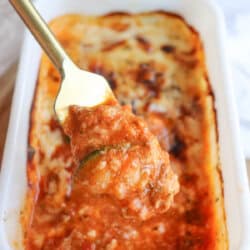 A fork holds a piece of stuffed pepper above a baking dish filled with a savory, tomato-based sauce. Herbs and melted cheese suggest its a freshly cooked delight, reminiscent of single-serving zucchini lasagna, ready to savor.