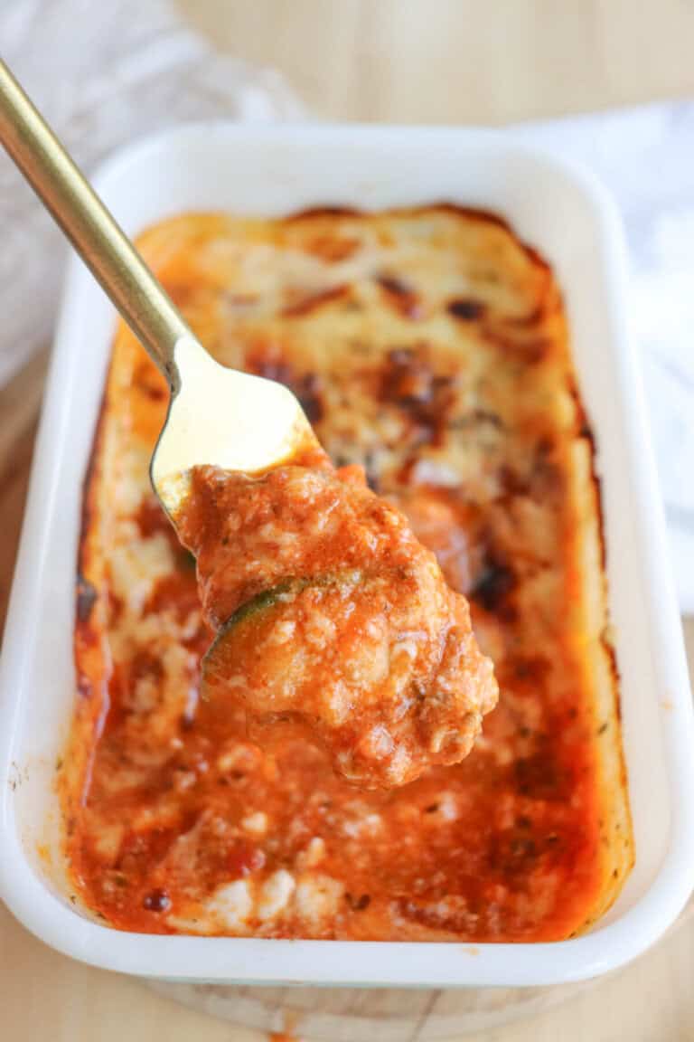 A fork holds a piece of stuffed pepper above a baking dish filled with a savory, tomato-based sauce. Herbs and melted cheese suggest its a freshly cooked delight, reminiscent of single-serving zucchini lasagna, ready to savor.