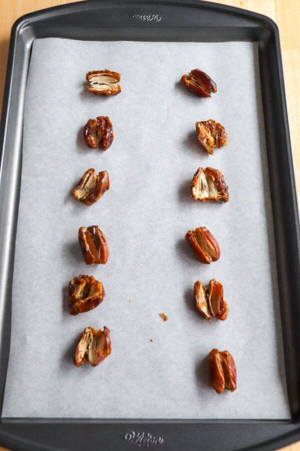 A baking sheet lined with parchment paper holds two neat rows of pitted dates, ready for smashing or further preparation.