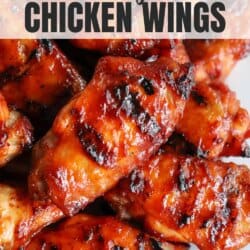 Close-up of barbecue grilled chicken wings, glistening with a charred, caramelized glaze. The texture appears crispy and flavorful, with visible grill marks.