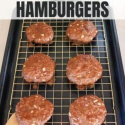 Raw hamburger patties on a wire rack atop a baking sheet, ready to cook. Text at the top reads, How to Bake Hamburgers, and a website URL is at the bottom. A small green plant is visible in the background.
